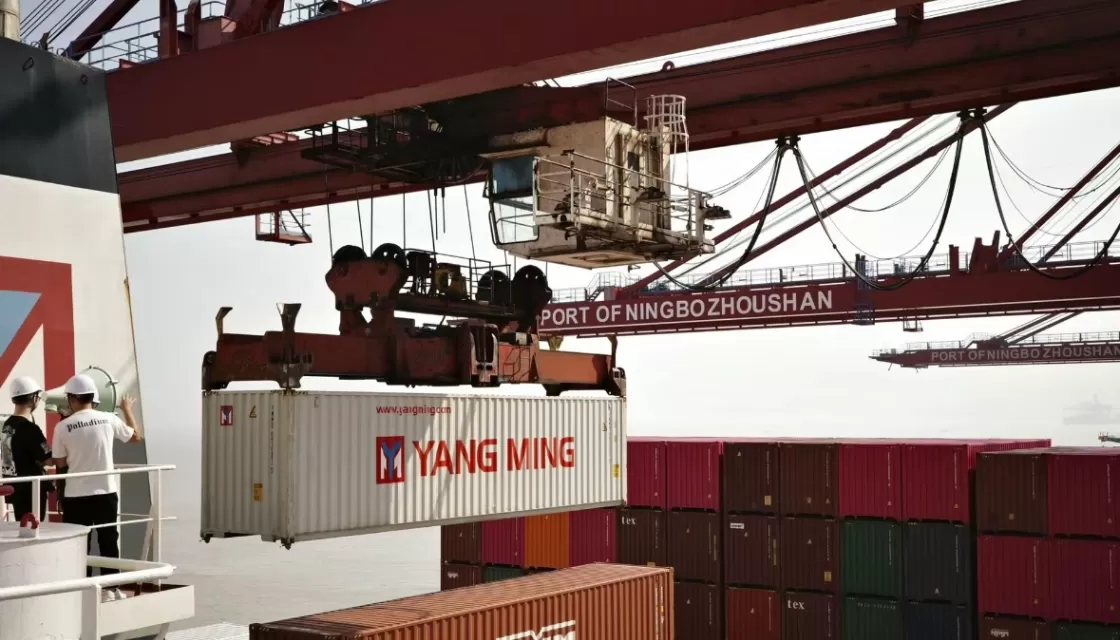 A container is being lifted by a crane at the Port of Ningbo Zhoushan, with workers observing.